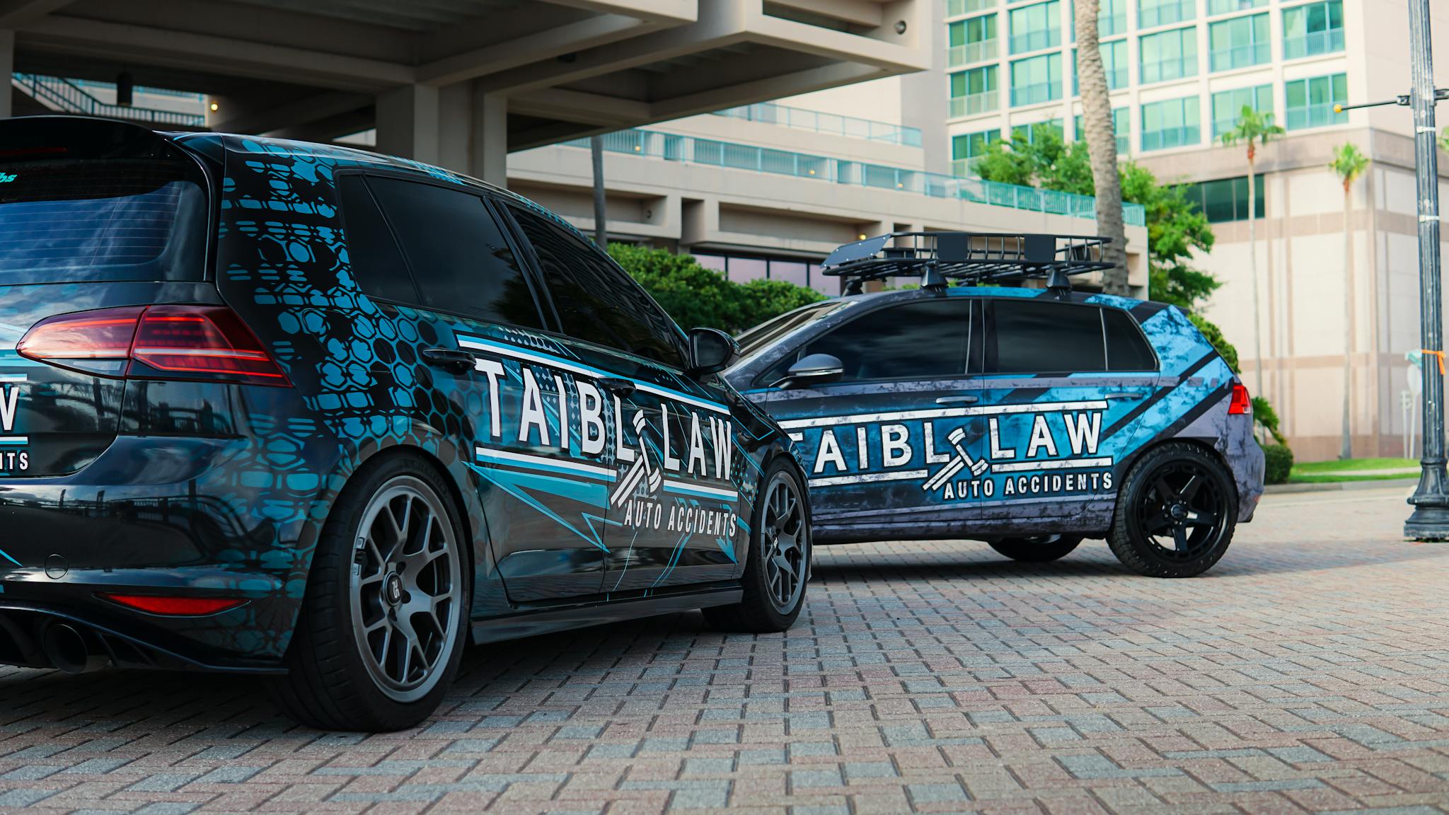 Street view of two Volkswagen Golfs with custom wraps displaying company advertising parked outdoors.