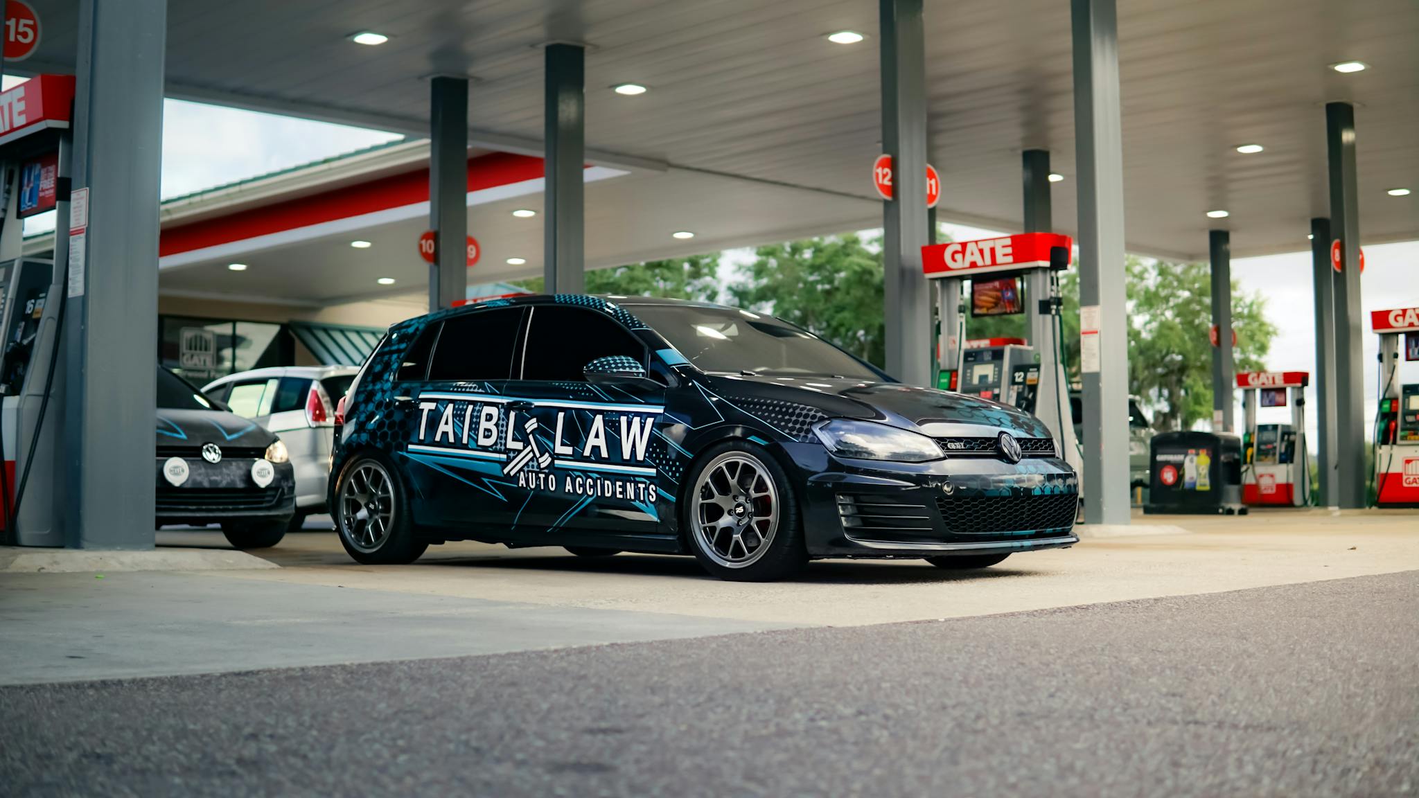 Volkswagen car with custom wrap parked at a gas station.